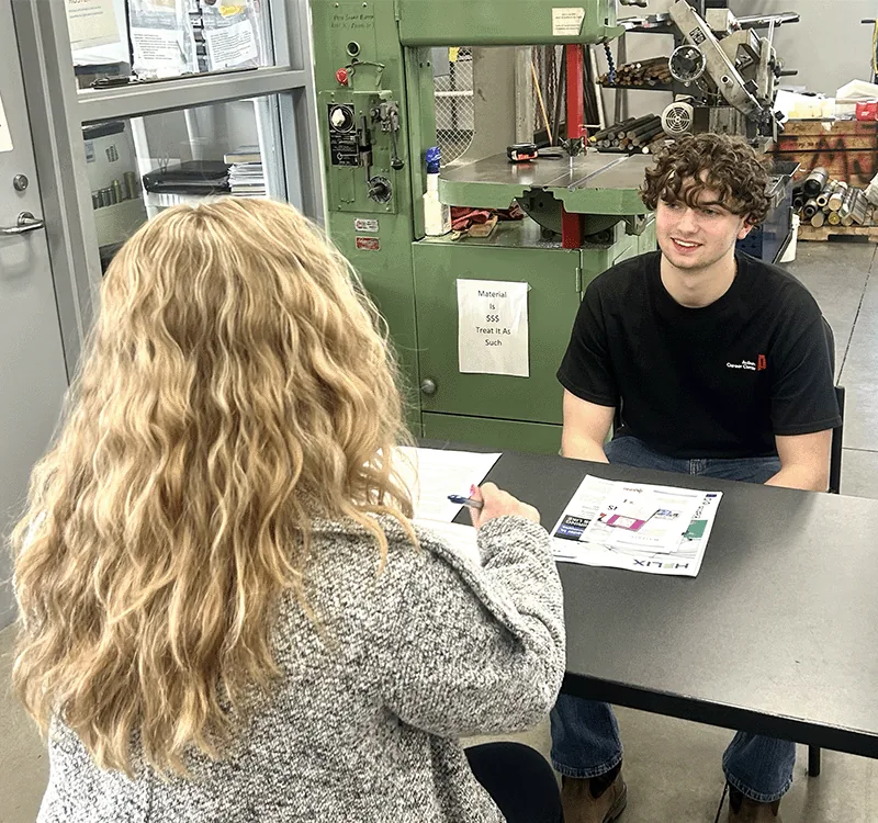 A Just In Time Staffing recruiter interviewing a job applicant beside a machine shop bandsaw